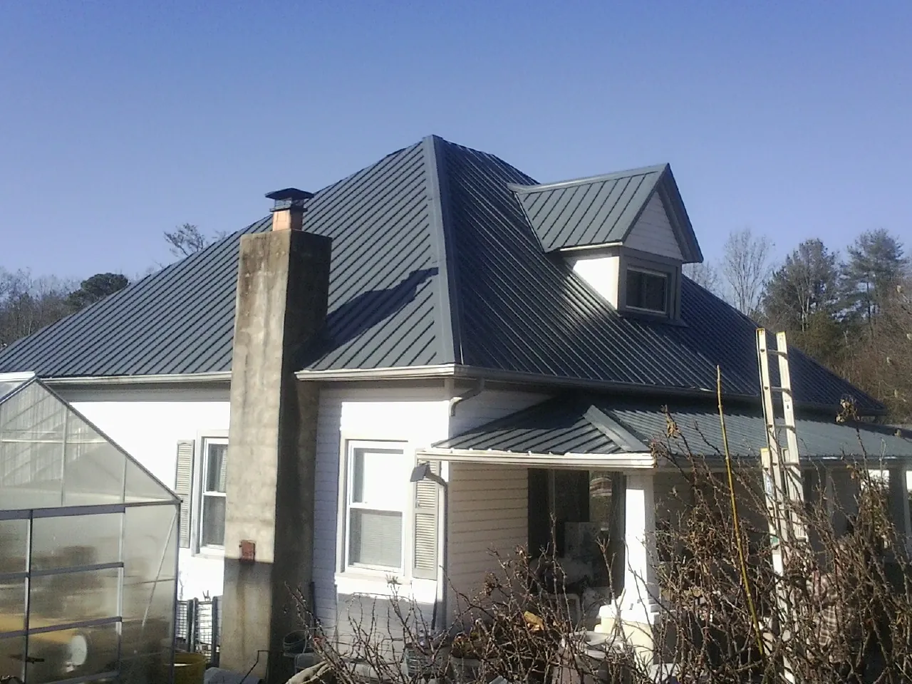 Dark blue standing seam metal roof on a white farmhouse with dormer — Slate & Tile Roof Repair by Roofing Brothers in Wildwood