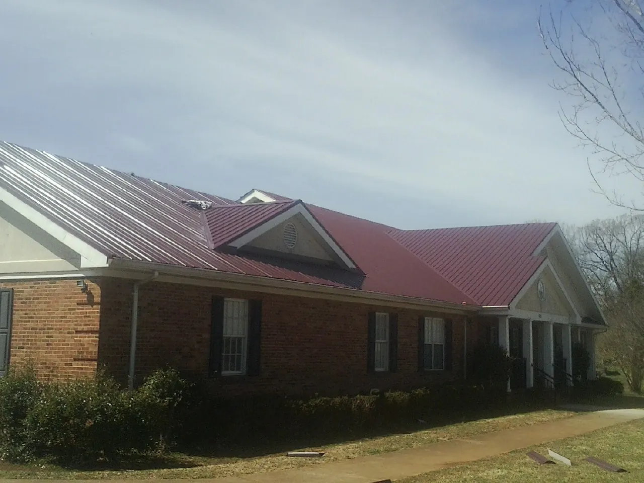 Red metal roof with gabled entries on a long brick building, from a Hail Damage Roof Repair job in Wildwood